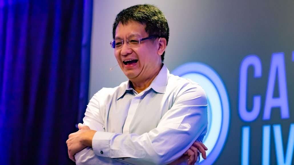 Close up of Ron Choong laughing in front of the Catalyst Live logo